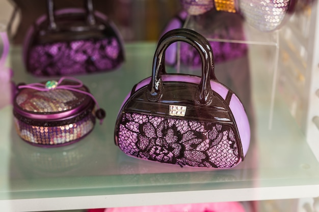 A decorative miniature handbag ornament with black lace over lavender, displayed on a glass shelf with other purple items.