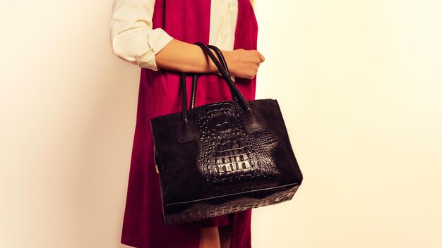 Close-up of a woman in a maroon top holding an elegant black tote bag featuring a glossy crocodile-effect panel.
